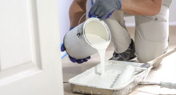 man pouring white paint into tray