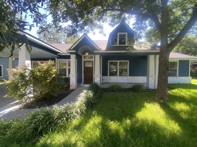 front corner of blue house with white trim and covered front porch and yard