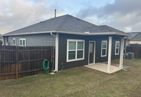 rear of dark grey painted house with covered doorway and wooden fence attached