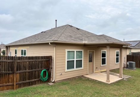 rear of tan house with covered doorway and wooden fence attached
