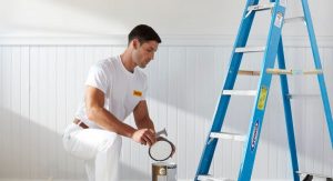 CertaPro Painters painter in painters whites next to a lader and white walls opening a paint can.