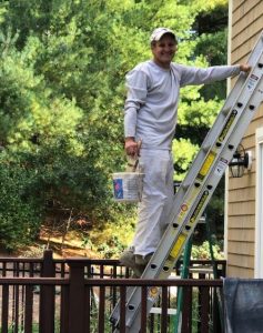 Painter on ladder painting shingles of Duxbury home in the fall.
