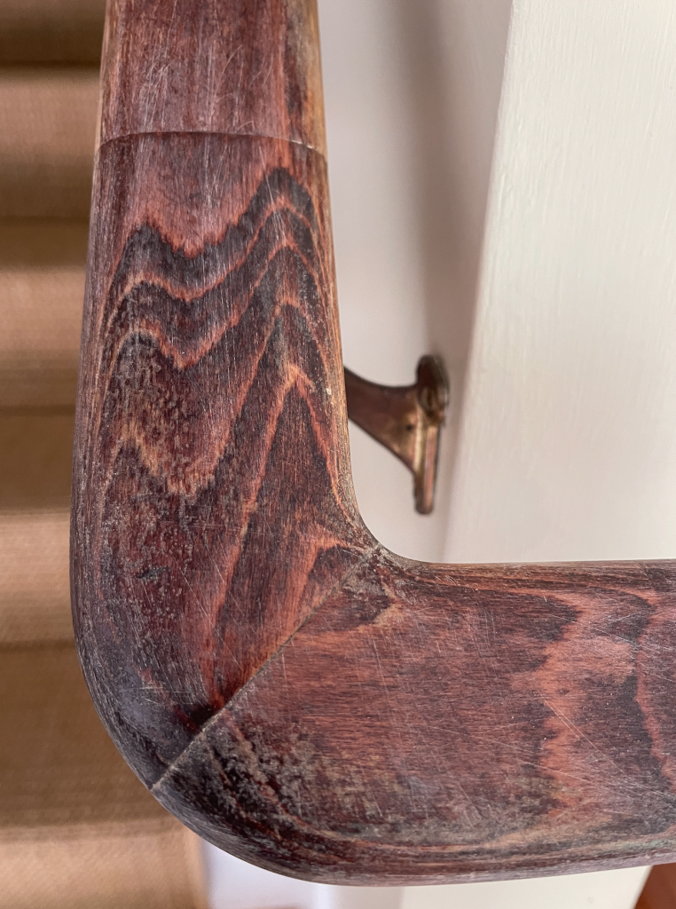 Close up of a wood banister that has been de-glossed by sanding it - scratches are visible from the sanding