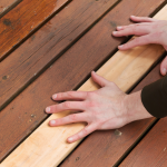 2 hands replacing an unfinished piece of mahogany wood on a deck floor