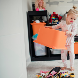 Toddler dumping toys from a bucket in a room with gray walls