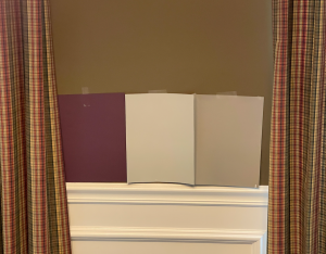 Large paint color samples in plum and beige are displayed on a brown wall with checkered curtains