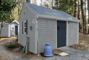 Paint rendering of a shed in gray with a dark door.