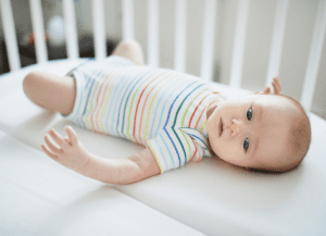 Baby in crib with striped shirt on laying on his back.