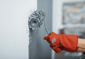 Paint roller painting a blue gray wall white.