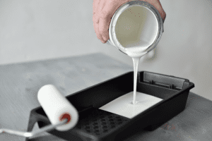 White paint being poured into a black paint tray with a paint roller off to the side.