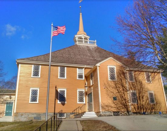 Shingled church in Hingham Massachusetts with a flagpole in front.
