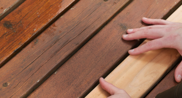 2 hands replacing an unfinished piece of mahogany wood on a deck floor
