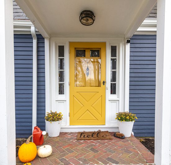 yellow painted front door with white trim on blue home