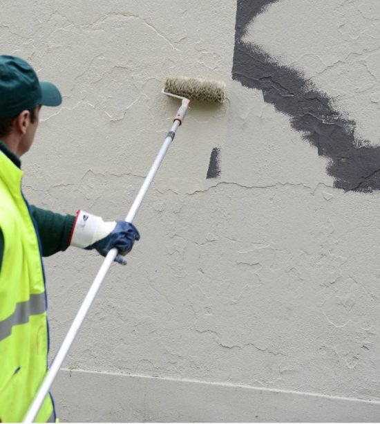 man painting over graffiti on exterior wall