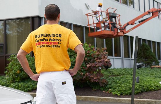 Painter in Gold CertaPro Painters shirt supervising painters on a lift.