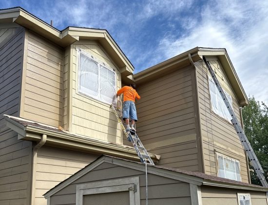 person on ladder painting upper level of house exterior