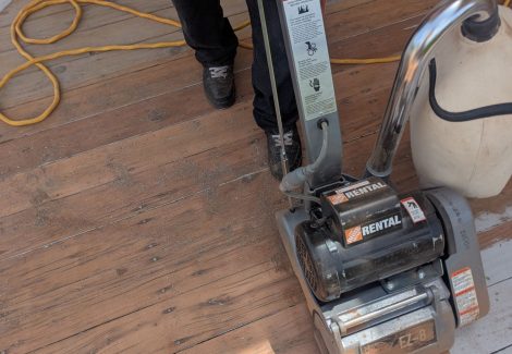 painter stripping old paint from wooden deck with equipment