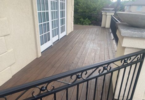 stained wooden deck against house with black metal railing