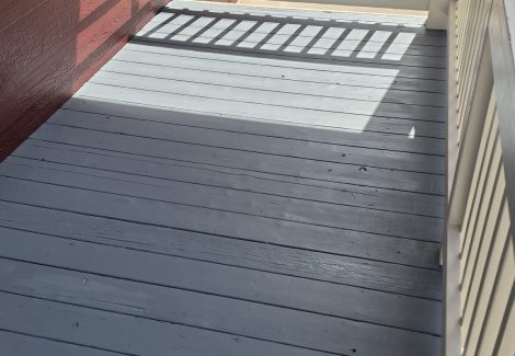 attached wooden porch painted grey with white rail against dark red siding