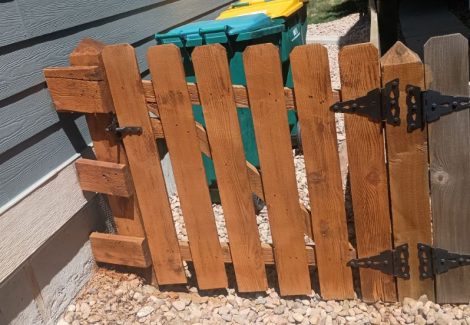 stained fence gate surrounding refuse bins against house