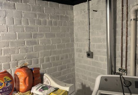 washer & dryer in room with whitewashed brick walls and black painted ceiling beams