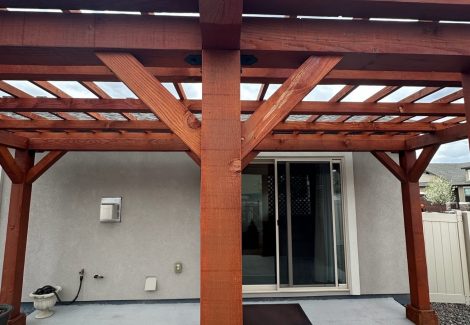 stained wooden pergola over patio behind home