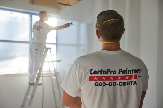 CertaPro Team Member observing another team member painting an interior office wall