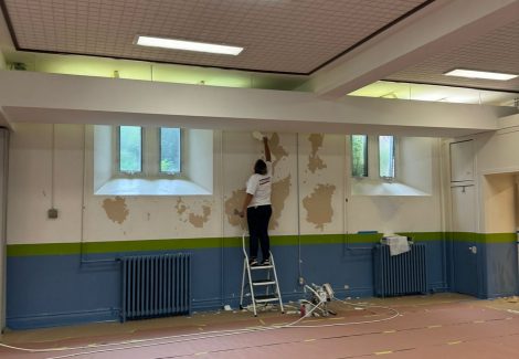 painter priming a gymnasium wall for repainting