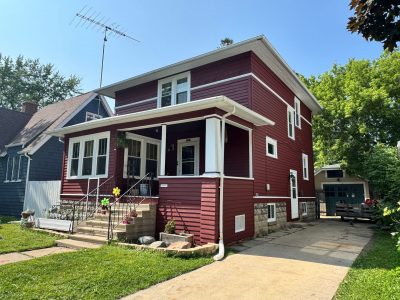 street view of home with dark red painted wood siding and white trim