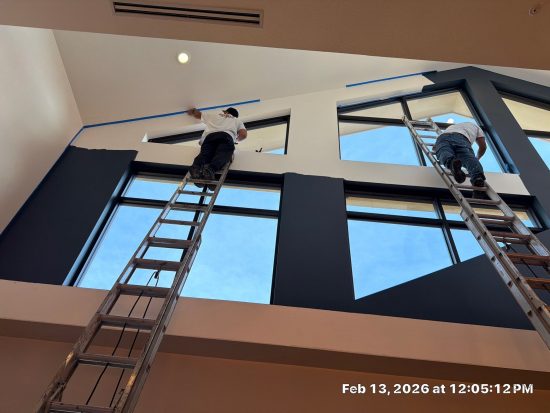 painters on ladders painting high white walls blue