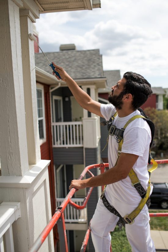 CertaPro Team Member Standing on a Lift Painting a Home Owner's Association Apartment Exterior