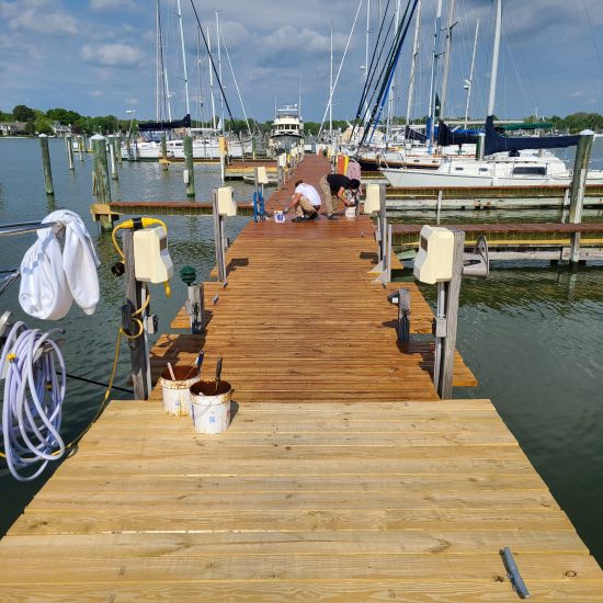 two painters wood staining a dock in Maryland with unstained wood in the foreground