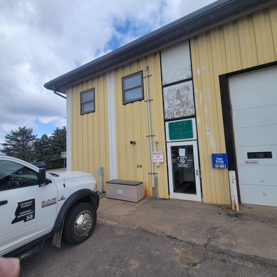 greyish yellow paint job done on commercial building with large white garage doors underneath gloomy weather in Le Center, Minnesota. A white car is parked in front of the building. Preview Image 4
