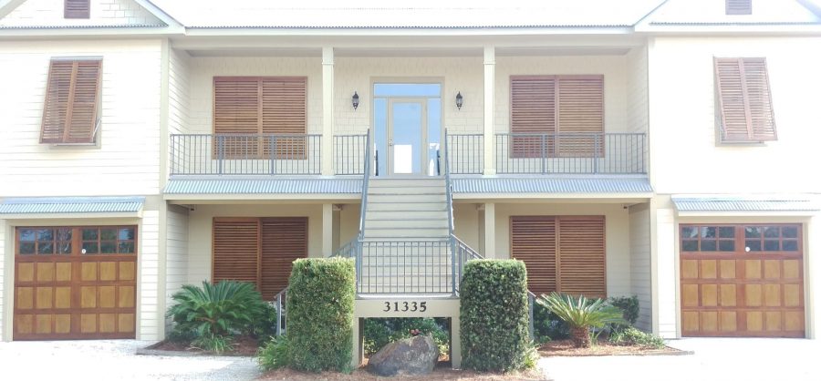 sidewalk view of residential property with stained wood garage doors and window shutters