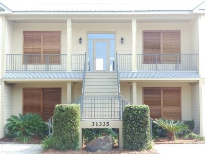 sidewalk view of residential property with stained wood garage doors and window shutters