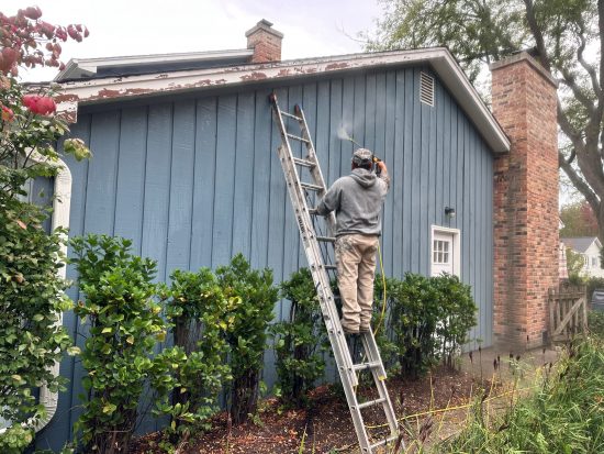 person on ladder spraying siding of house
