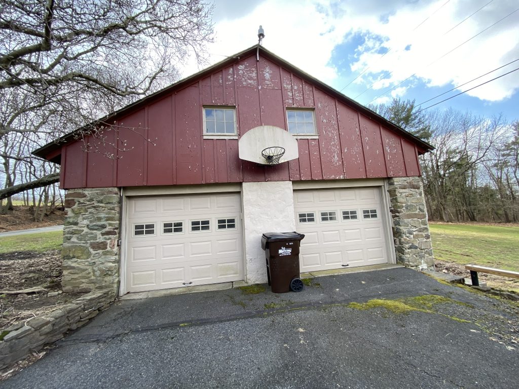 front of garage with basketball hoop, bottom half made of stone and top half maroon painted wood with a lot of wear and tear 