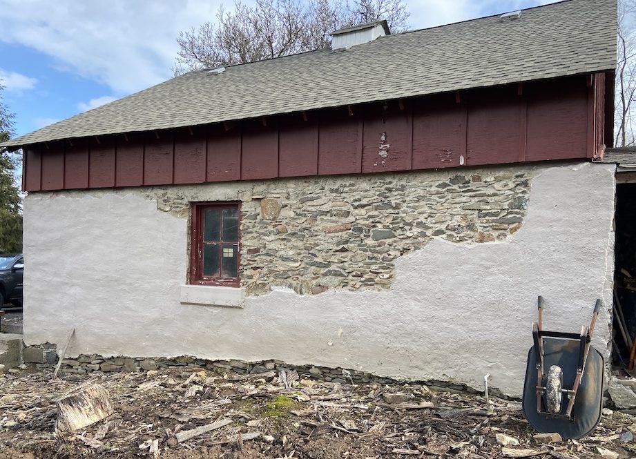 side of garage with stone and concrete base, maroon trim window, maroon painted wood and grey roof
