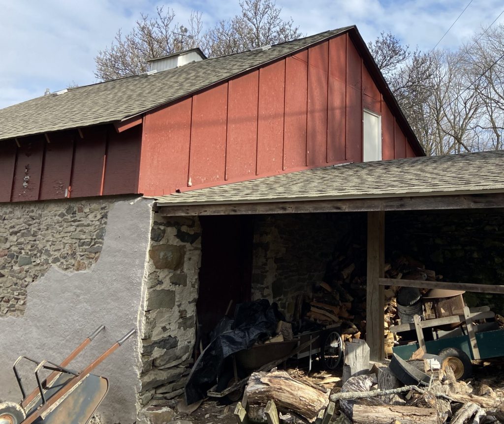 side of barn, bottom half concrete and stone, top half maroon wood with a dark grey roof