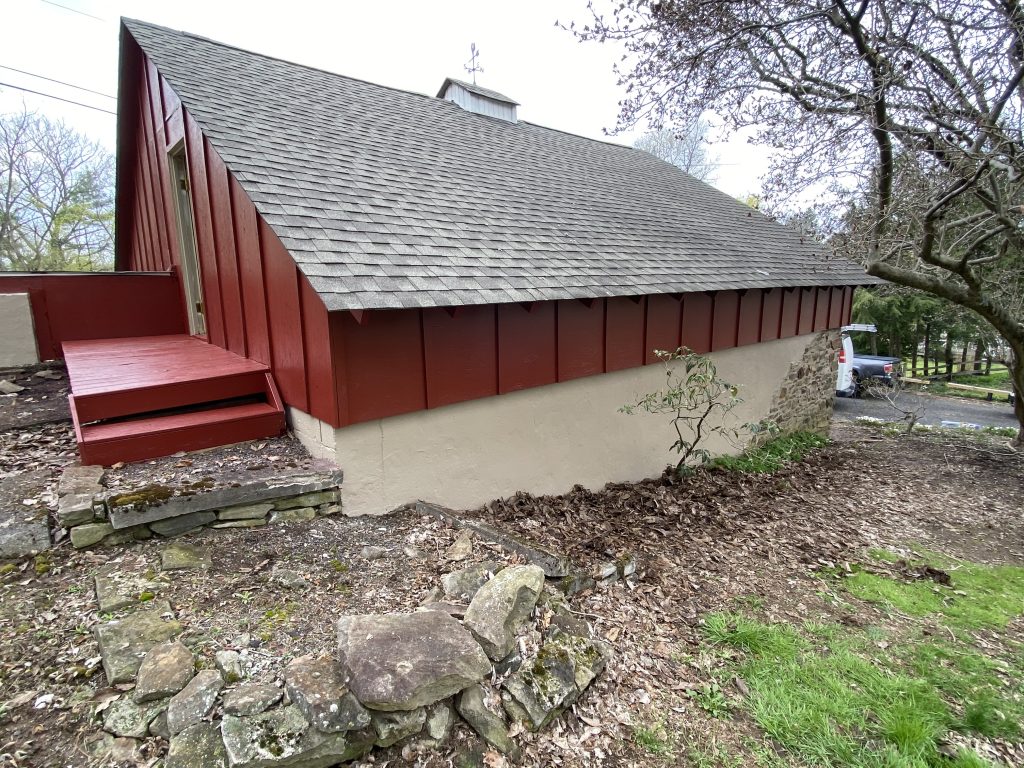 side of barn freshly painted maroon with a grey roof and tan concrete as the base
