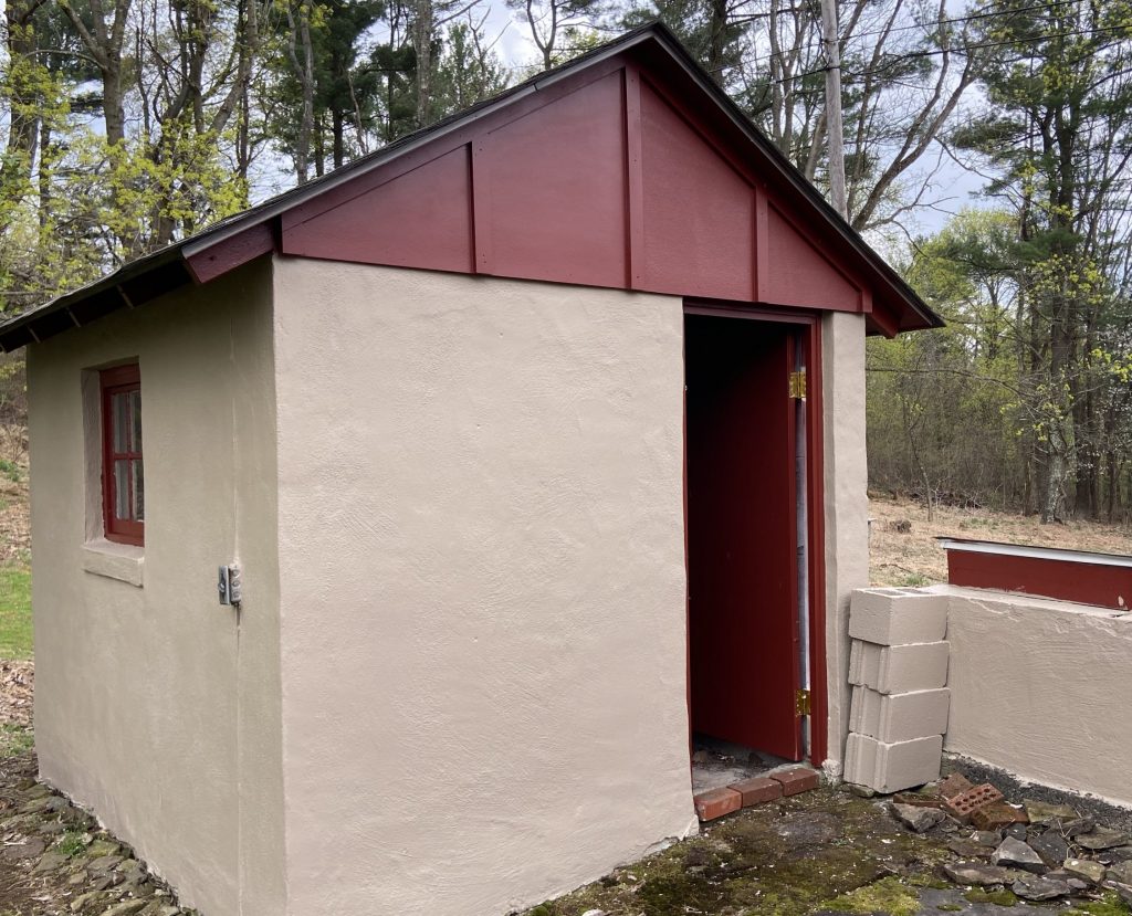 front of shed with tan cement, maroon painted door and maroon painted wood