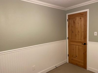 An interior bedroom with painted wainscoting and crown molding.