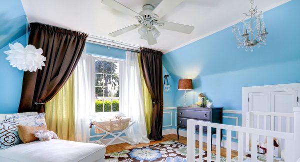 Bright cheerful nursery room interior with blue walls and hardwood floor. Room has crib, settee and cabinet