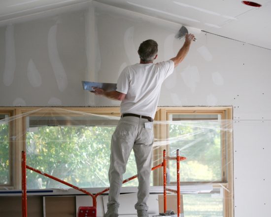 man painting drywall while on scaffolding