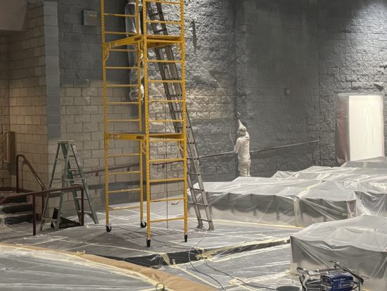 painter spraying auditorium interior wall during paint project
