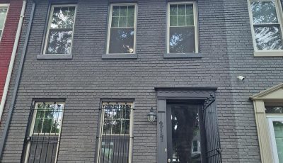 front exterior of grey painted brick townhouse with black door and trim