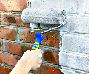 paint roller on brick exterior with white paint