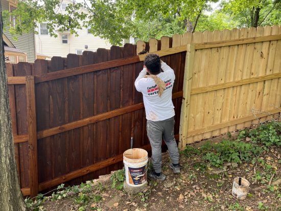 CertaPro Painters of Winston-Salem stain a large backyard fence perimeter.