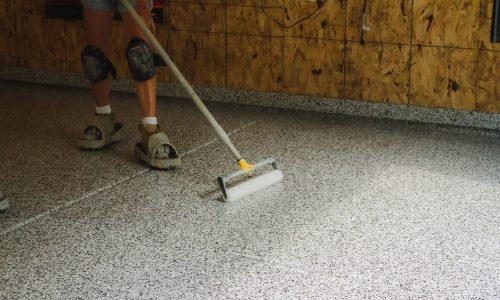 CertaPro Painters of Winston-Salem contractor painting an epoxy floor with a sealant in a home workshop.