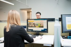 Image of employees working on a computer in a cubicle. 